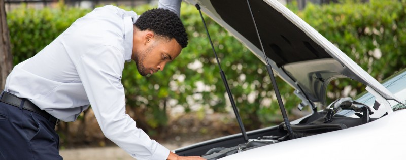 Closeup portrait, young man having trouble with his broken auto, opening hood trying to fix engine, isolated green trees outside background. Car won't start, dead battery